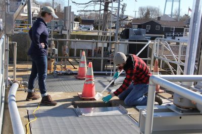Jake Madden, lab technician with Spinney Creek Shellfish, collects a water sample at the Mystic Wastewater Treatment Plant as Kristin DeRosia-Banick of the state Bureau of Aquaculture looks on.