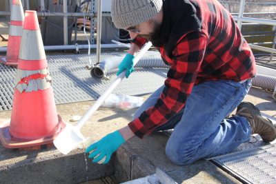Jake Madden collects a water sample at the Mystic Wastewater Treatment Plant that for a testing project that could open areas to shellfish farming.