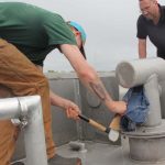 Fisherman Chad Davenport hammers a wedge into a leaking pipe to make an emergency repair as Steve Pigeon, commercial fishing safety examiner with the Coast Guard, looks on.