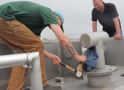 Fisherman Chad Davenport hammers a wedge into a leaking pipe to make an emergency repair as Steve Pigeon, commercial fishing safety examiner with the Coast Guard, looks on.