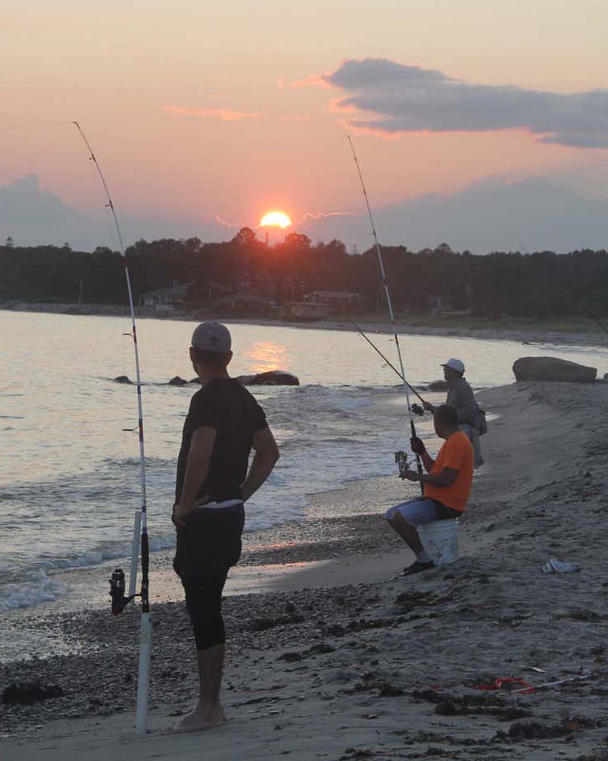 Fishermen with surf-casting poles watch the setting sun from the beach at Harkness Memorial State Park in Waterford on Aug. 22.