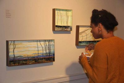 UConn student Annalisa Mudahy looks at three paper, metal and clay works created by artist Ashby Carlisle, "On a Clear Day," left; "Whispers in the March," center; and "On Shore Breeze," right.