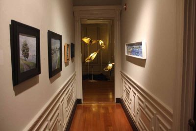 Scenes of the Avery Point campus done by members of the Connecticut Plein Air Painters Society are hung in a hallway leading to the room where "Ghost Whales," a work by Kristian Brevik, is displayed.