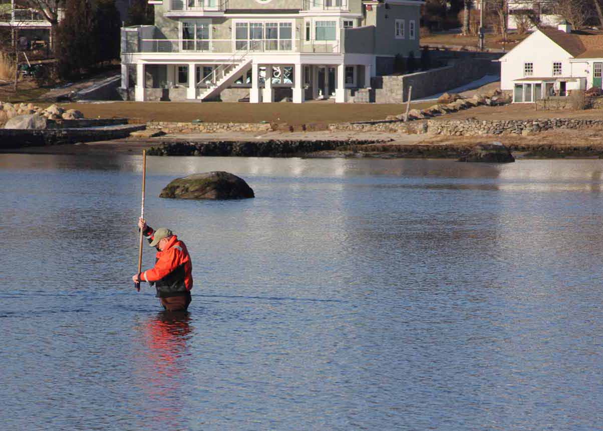 Don Murphy, chairman of the Stonington Shellfish Commission, lifts a water sample from one of the town's recreational shellfishing areas in the Mystic River at low tide on March 13.