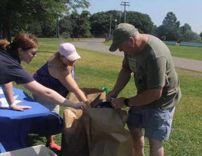 Volunteer Scott Shail, right, empties the trash he collected into a large paper bag as his wife Laura, Sunny Valley Preserve administrator for The Nature Consevancy, and Ireland Wilson, senior conservation instructor for the Mystic Aquarium, help hold the bag.