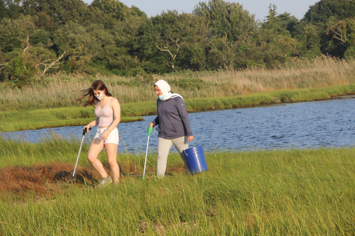 Katya Mirsky, left, and Massa Traboulsi, both juniors at Stonington High School, cross the marsh in search of trash.
