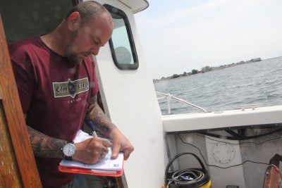 Rick Selen, research vessel engineer aboard the aquaculture bureau's vessel Sea Hawk, record information on the date, time and tidal conditions of each water sample.