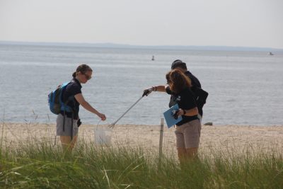 Lisa Jarosik, right, a dive volunteer at the Maritime Aquarium, places trash collected on the beach at Sherwood Island in a bucket held by Bridget Cevero, education manager at the aquarium. Among the items the pair picked up were flip-flops, several tubes of lip balm, large pieces of confetti and a cement trowel.