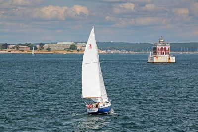 A sailboat passes close to Ledge Light at the mouth of the Thames River.