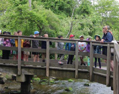 Flanders Elementary School teacher Laura Moore, right, leads her first-grade students across a bridge over Bride Brook in Rocky Neck State Park in East Lyme, CT.
