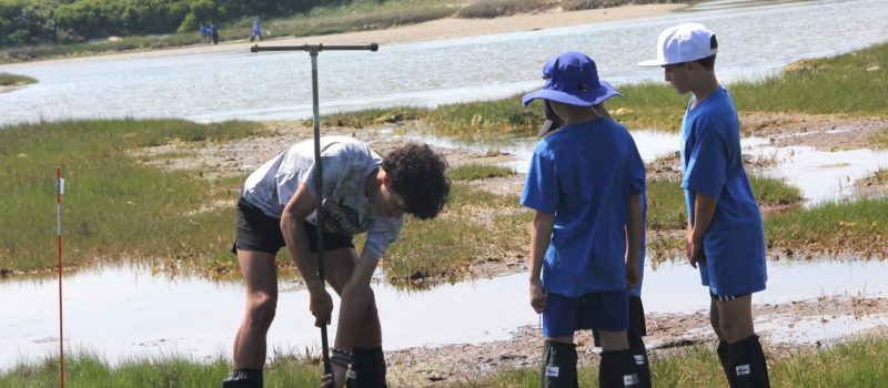 Waterford High School student Caydin Martinez, left, shows two of the approximately 370 Waterford elementary school students how to measure the depth of marsh sediment during Marine Science Day at Waterford Town Beach on June 3.