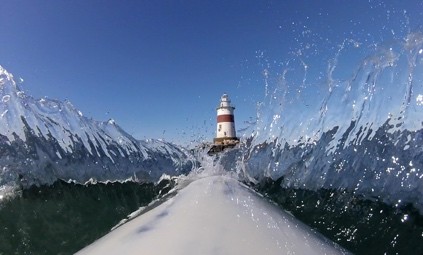 Image of a lighthouse seen over the bow of a kayak with waves splashing