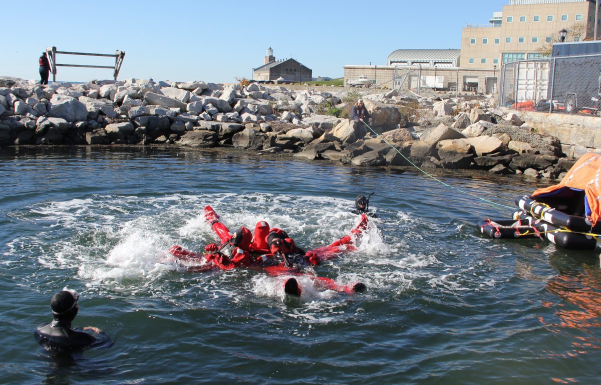 Students practice swimming kicking and splashing in a star formation to alert rescue helicopters before swimming to to the life raft, right, as safety divers look on.
