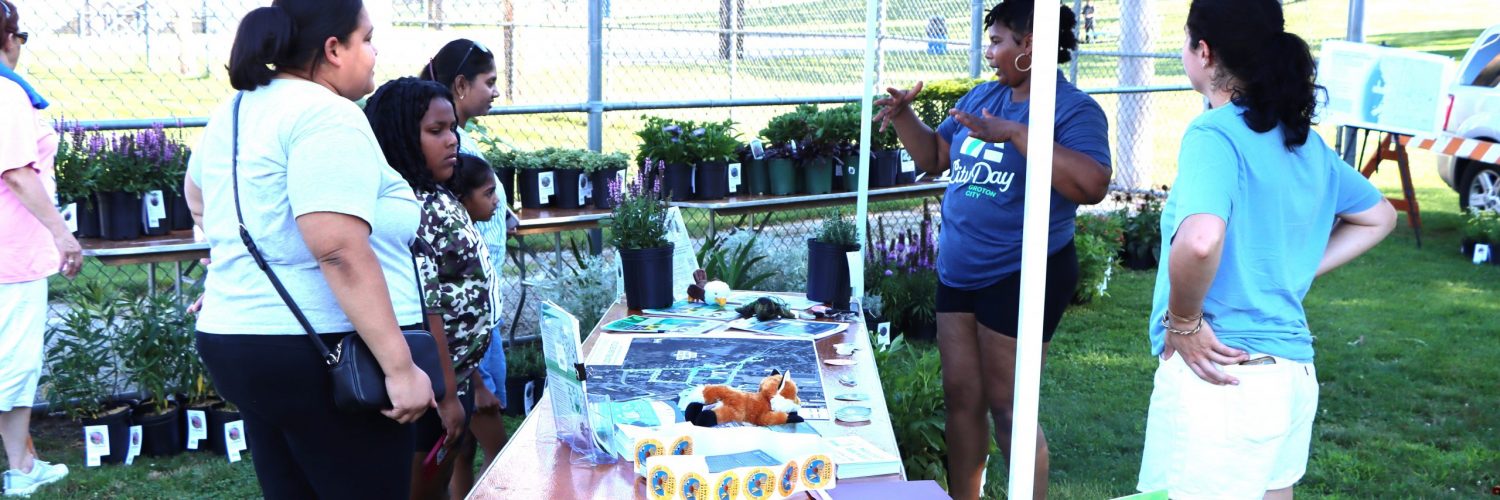 Groton City Economic Development Manager Cierra Patrick, second from right, talks to Groton City Day participants at the city's resiliency project display, where residents could get free pollinator plants, rain barrels and other items.